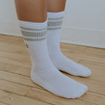 A pair of white tall sport breathable bamboo socks with striped patterns on the cuff being worn
