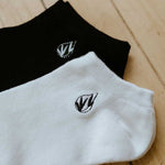 a pair of white + black everyday ankle bamboo socks closeup on caroquilla logo 